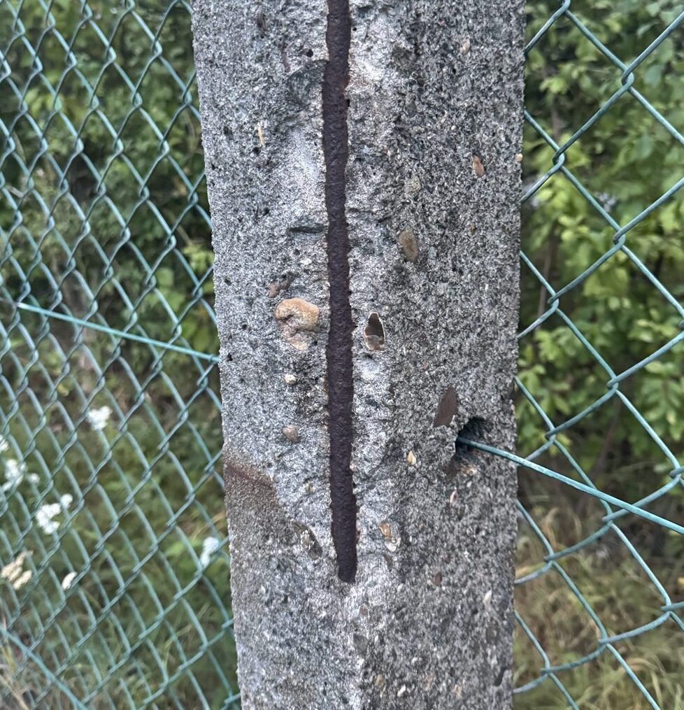Concrete post with corrosion-related spalling and exposed rusted reinforcing steel.