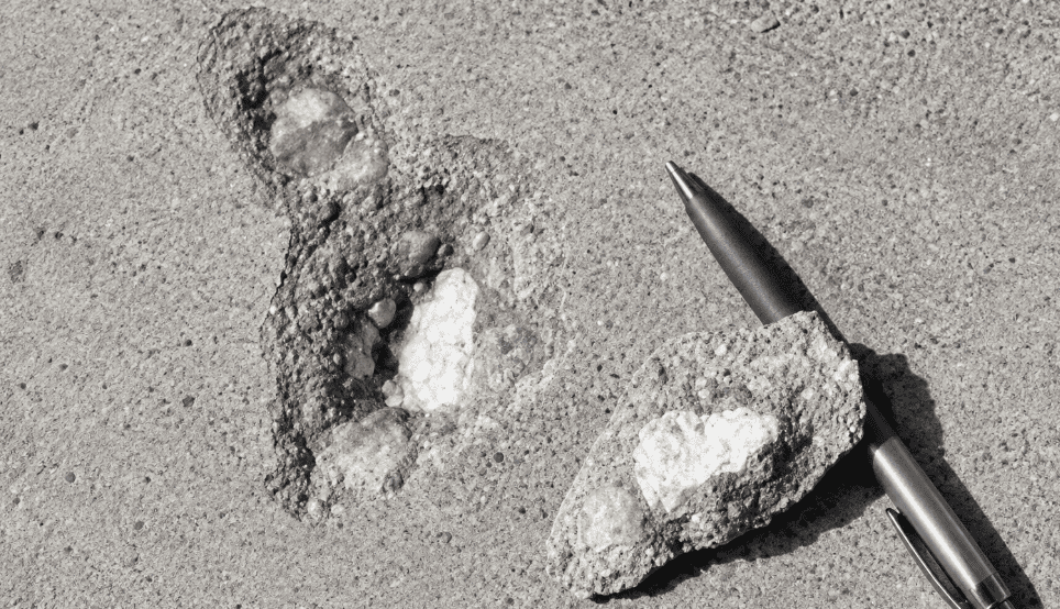Concrete popout showing a cone-shaped surface cavity, exposed aggregate, and the broken concrete fragment beside the damaged area.