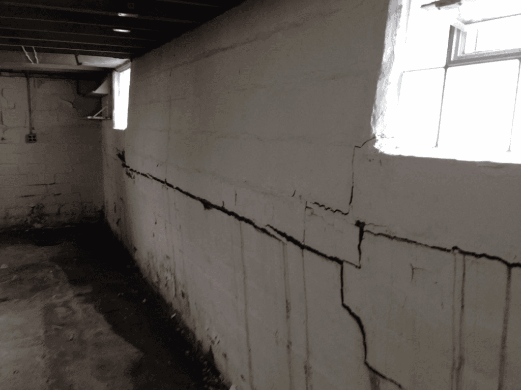 Horizontal crack running through a concrete block basement wall with additional vertical cracking and moisture staining near the floor.